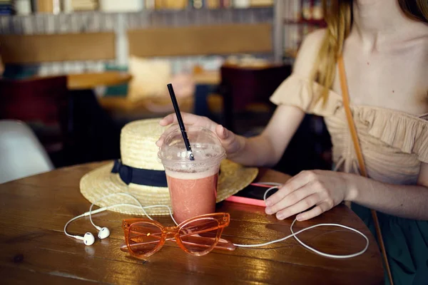 一个女人坐在餐馆里，带着耳机和一杯新鲜的玻璃杯，享受休闲娱乐 — 图库照片