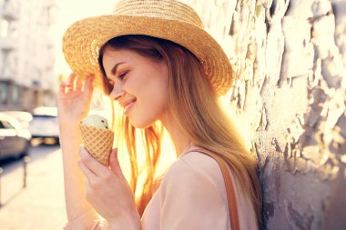 Kadın dışarıda dondurma yiyor, güneşli gündüzleri yürüyor.