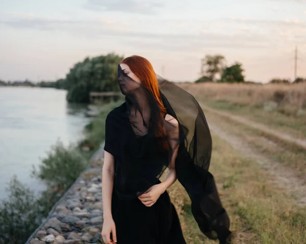 Uma mulher em um vestido com um lenço preto ao ar livre perto do rio — Fotografia de Stock