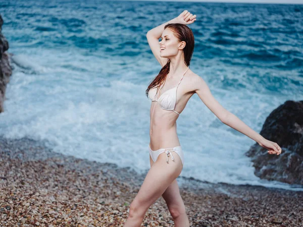 Una donna snella in costume da bagno bianco gesti con le mani sulla riva dell'oceano — Foto Stock