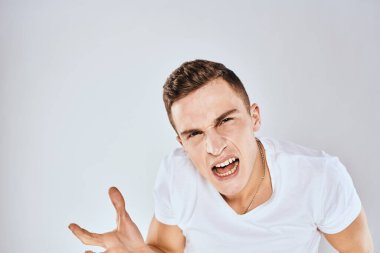 Elleriyle hareket eden duygusal bir adam. Yüz ifadesi hoşnutsuz. Beyaz tişört kesilmiş.