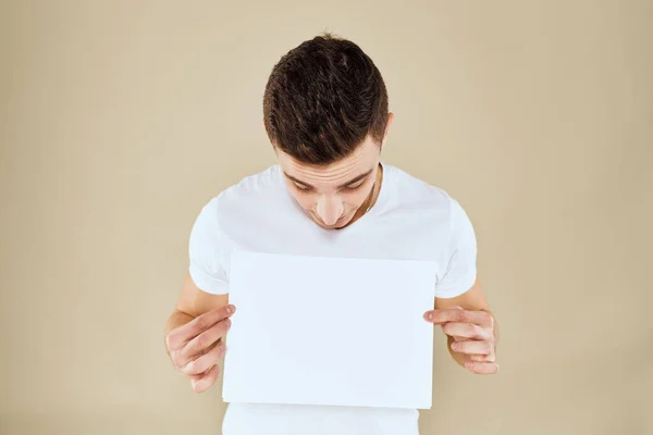 Homme en blanc t-shirt feuille de papier dans les mains Copier Espace vue recadrée fond beige — Photo