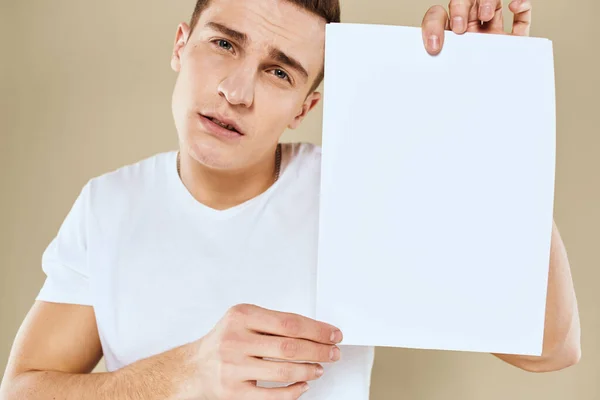 Man in wit t-shirt vel papier in handen kopiëren ruimte bijgesneden weergave beige achtergrond — Stockfoto