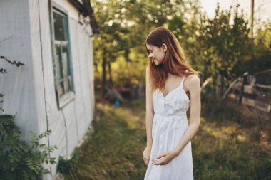 Binanın yakınında beyaz bir elbise içinde mutlu bir kadın ve arka planda ağaçlar.