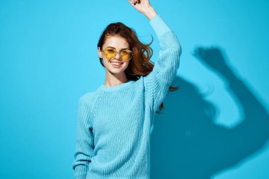 Mavi kazaklı güzel bir kadın. Sarı güneş gözlüklü. Gülümsüyor.