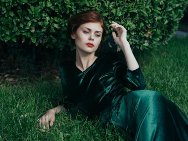 Yeşil elbiseli güzel bir kadın çimlerin üzerinde gotik stil maskeli cazibesiyle yatıyor.