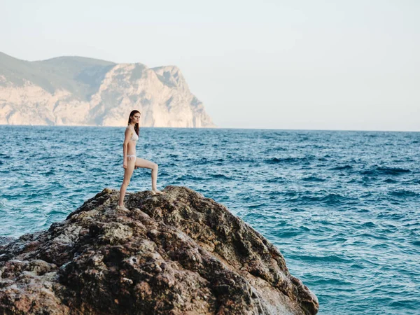 Woman stands on a high rock in nature near the sea and a mountain in the backgroun — Stock Photo, Image