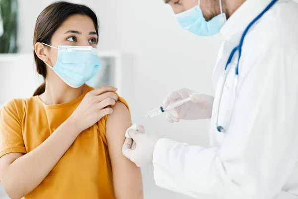 Vista lateral del médico inyectando la vacuna en el hombro del paciente con máscara médica en la epidemia hospitalaria —  Fotos de Stock