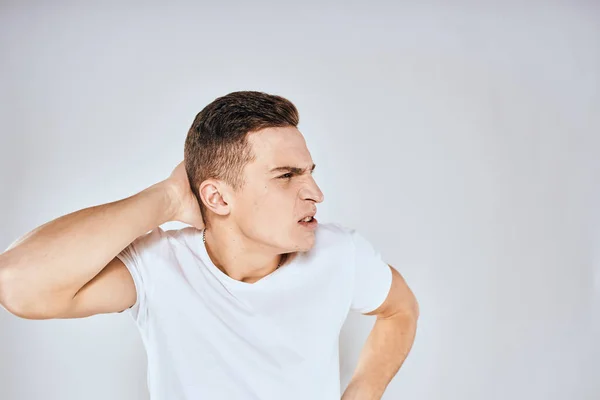 Emotional man in a white t-shirt holds his hand on his face light background — Stock Photo, Image