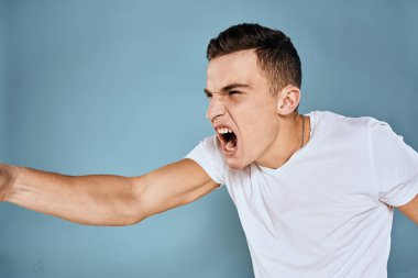 Erkek, duyguları ile hareket eder. Beyaz tişört yüz ifadesi mavi arka plan.