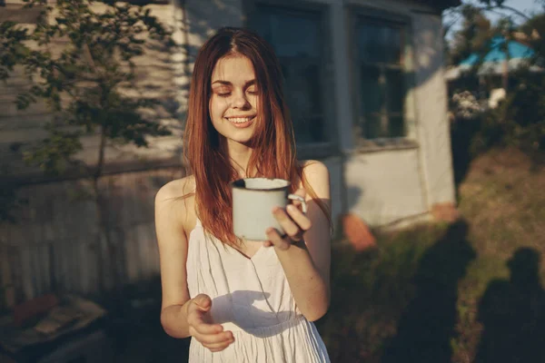 Femme heureuse avec tasse de fer à l'extérieur dans le jardin près du bâtiment de lumière — Photo