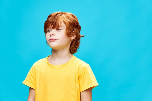 可愛いです男の子見ますザ · サイド黄色のTシャツクロップドビュー青の背景 — ストック写真