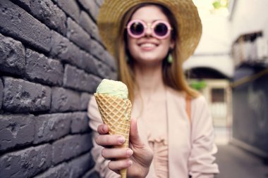 Güneş gözlüklü neşeli kadın ellerinde dondurmayla dışarıda siyah tuğlalı Wall Street tarzı