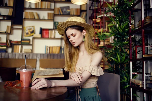 戴帽子的女人坐在咖啡店里喝酒看书度假 — 图库照片