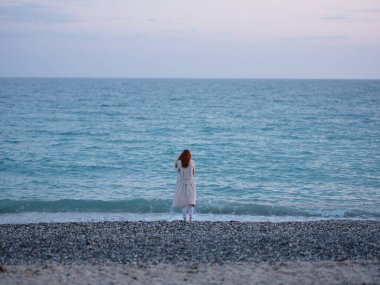 Okyanusun kıyısında beyaz pantolonlu bir kadın.