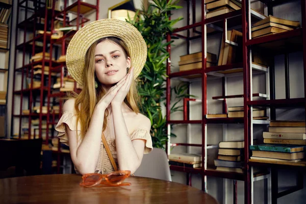 Belle femme dans un chapeau assis à une table dans un café livre de vacances amusant — Photo