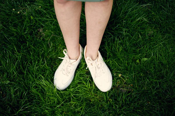 Női lábak fehér tornacipő zöld fű séta szabadban — Stock Fotó