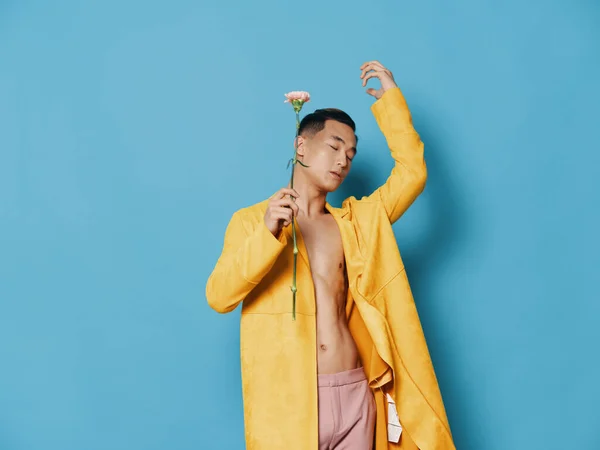 Asiatisk kille med en blomma i händerna och en gul rock blå bakgrund — Stockfoto