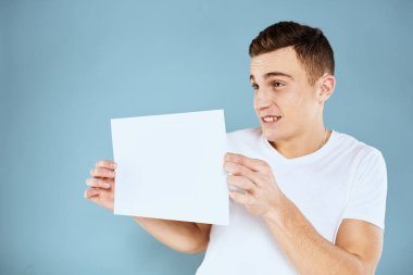 Beyaz tişörtlü bir adam elinde mavi arkaplan fotokopisini gösteren bir sayfa kağıt duygu tutuyor.