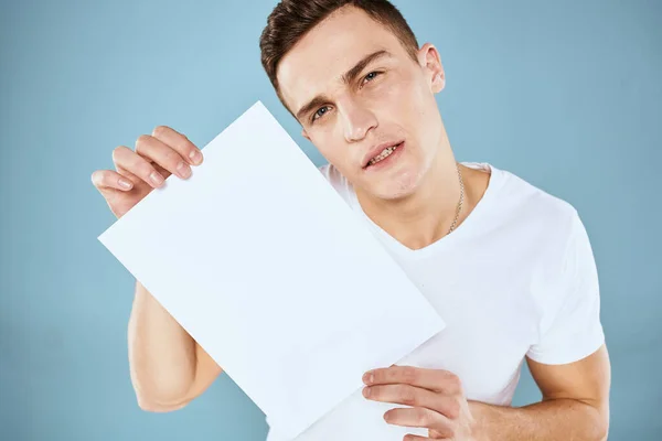 Een man in een wit t-shirt heeft een vel papier kopieerruimte — Stockfoto