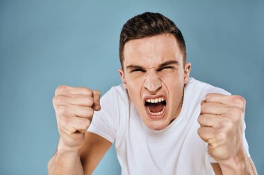 Erkek, duyguları ile hareket eder. Beyaz tişört yüz ifadesi mavi arka plan.