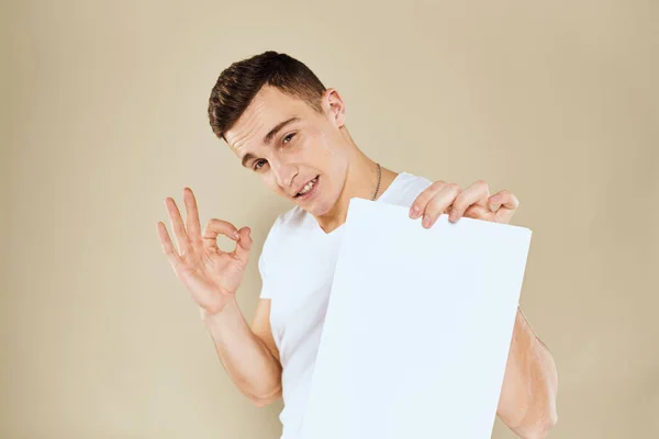 Man in white t-shirt sheet of paper in hands Αντιγραφή Χώρος περικοπεί προβολή μπεζ φόντο — Φωτογραφία Αρχείου