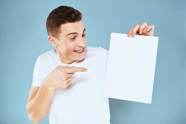 Homme tenant une feuille de papier dans ses mains blanc t-shirt recadré vue fond bleu — Photo