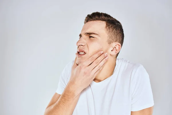 Uomo emotivo in una t-shirt bianca tiene la mano sul suo viso sfondo leggero — Foto Stock