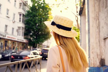 Şapkalı bir kadın güneşli bir günde şehirde yürüyor.