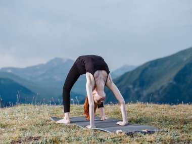 İnce bir kadın yogayla meşgul. Dağlarda tayt ve tişörtle.