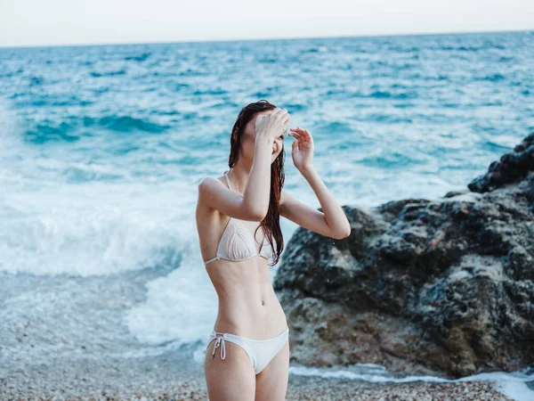 Una donna snella in costume da bagno bianco vicino all'oceano e schiuma bianca spruzzata tra le onde — Foto Stock