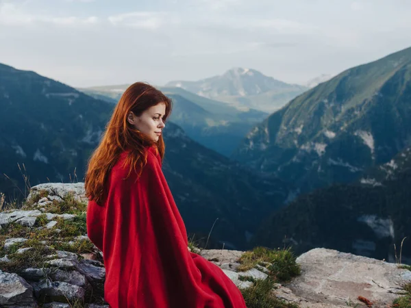 Kobieta siedzi na kamieniach pokryta czerwonym kocem w górach. — Zdjęcie stockowe
