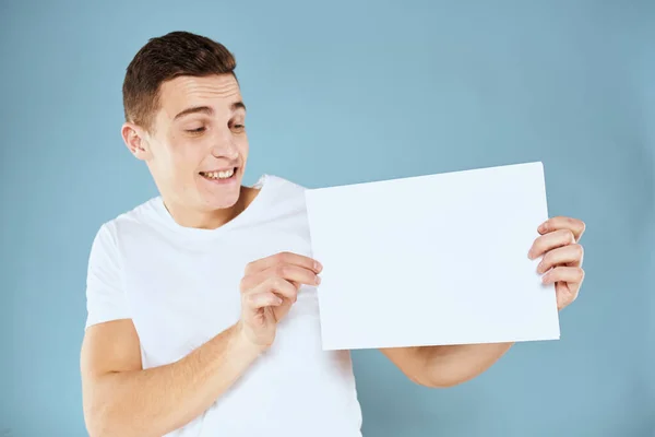 Man holding a sheet of paper in his hands white t-shirt cropped view blue background — Stock Photo, Image
