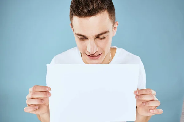 A man in a white t-shirt holds a sheet of paper copy space — Stock Photo, Image