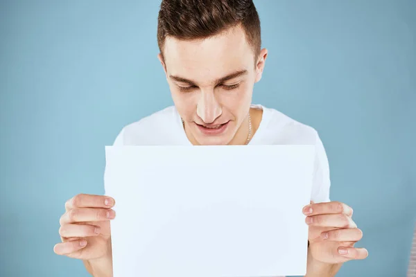 Een man in een wit t-shirt heeft een vel papier kopieerruimte — Stockfoto