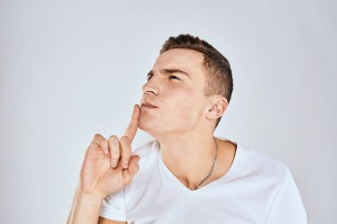 Beyaz tişörtlü duygusal bir adam elini arka planda tutuyor.