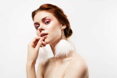 Güzel bir kadın parlak makyaj, tüylü küpeler, çıplak omuzlar, temiz bir cilt.