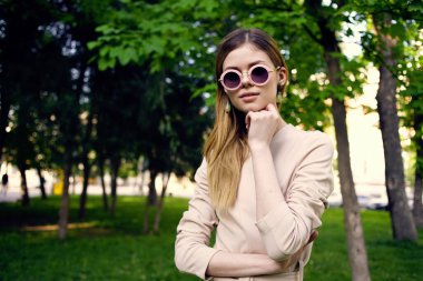 Yeşil ağaçların arasında güneş gözlüklü güzel bir kadın seyahat ediyor.