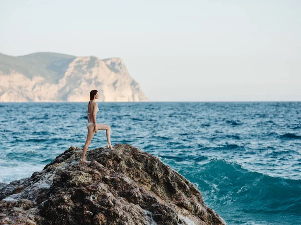 Woman stands on a high rock in nature near the sea and a mountain in the backgroun — Stock Photo, Image