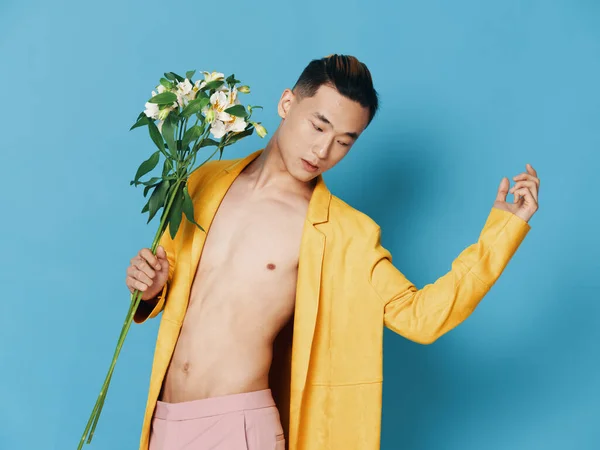 korean man with bouquet of flowers in yellow coat gesturing with hands cropped view