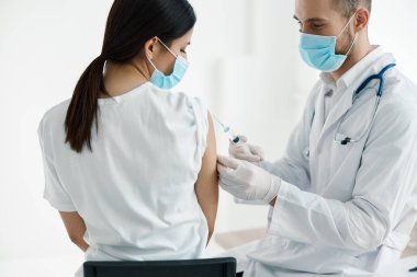 Tıbbi maskeli doktor kadın omuz salgını hastanesine aşı enjekte ediyor.