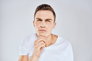 Beyaz tişörtlü duygusal bir adam elini arka planda tutuyor.