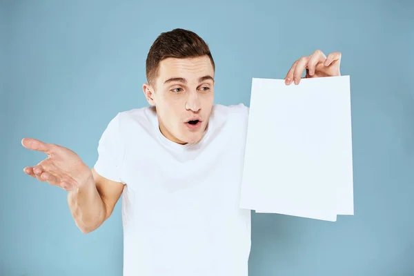 Man met een vel papier in zijn handen wit t-shirt bijgesneden uitzicht blauwe achtergrond — Stockfoto