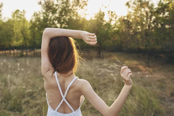 Retrato de una mujer feliz en un vestido de sol en un campo año de detrás de los árboles puesta de sol —  Fotos de Stock