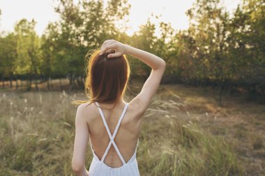 Mutlu bir kadının portresi bir tarlada güneşli bir elbise içinde gün batımında ağaçların arkasından.