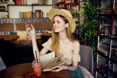 Şapkalı güzel bir kadın, elinde kitapla kafede tatil okuyor.