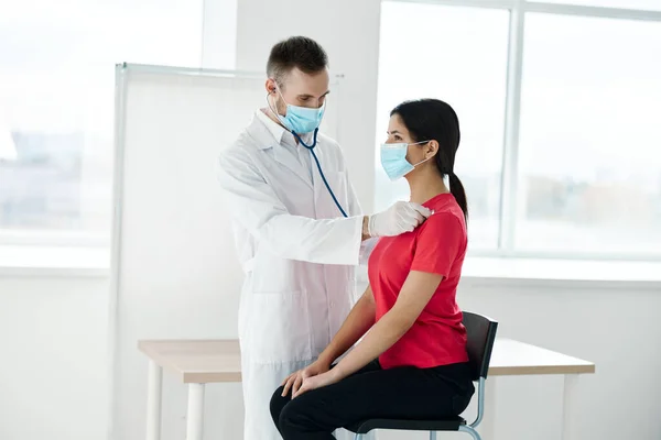 Un medico in maschera medica si trova accanto a una donna in una t-shirt rossa esame toracico respirazione polmoni covid — Foto Stock