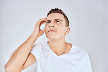 Beyaz tişörtlü duygusal bir adam elini arka planda tutuyor.