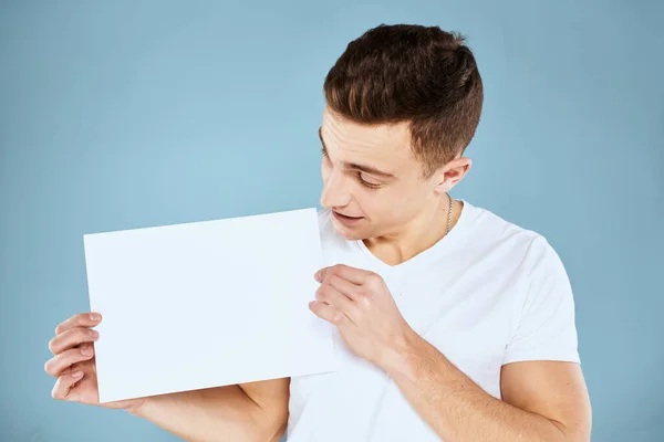 A man in a white t-shirt holds in his hands a sheet of paper emotions cropped view of a blue background Copy Space — Stock Photo, Image