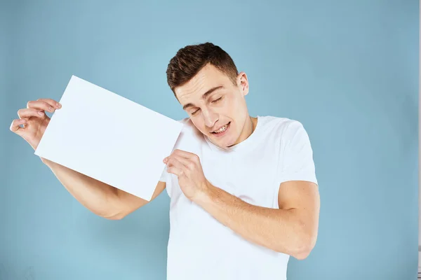 Een man in een wit t-shirt heeft een vel papier kopieerruimte — Stockfoto